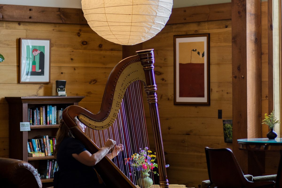 Patricia playing her pedal harp in a timber-framed room under a paper lantern