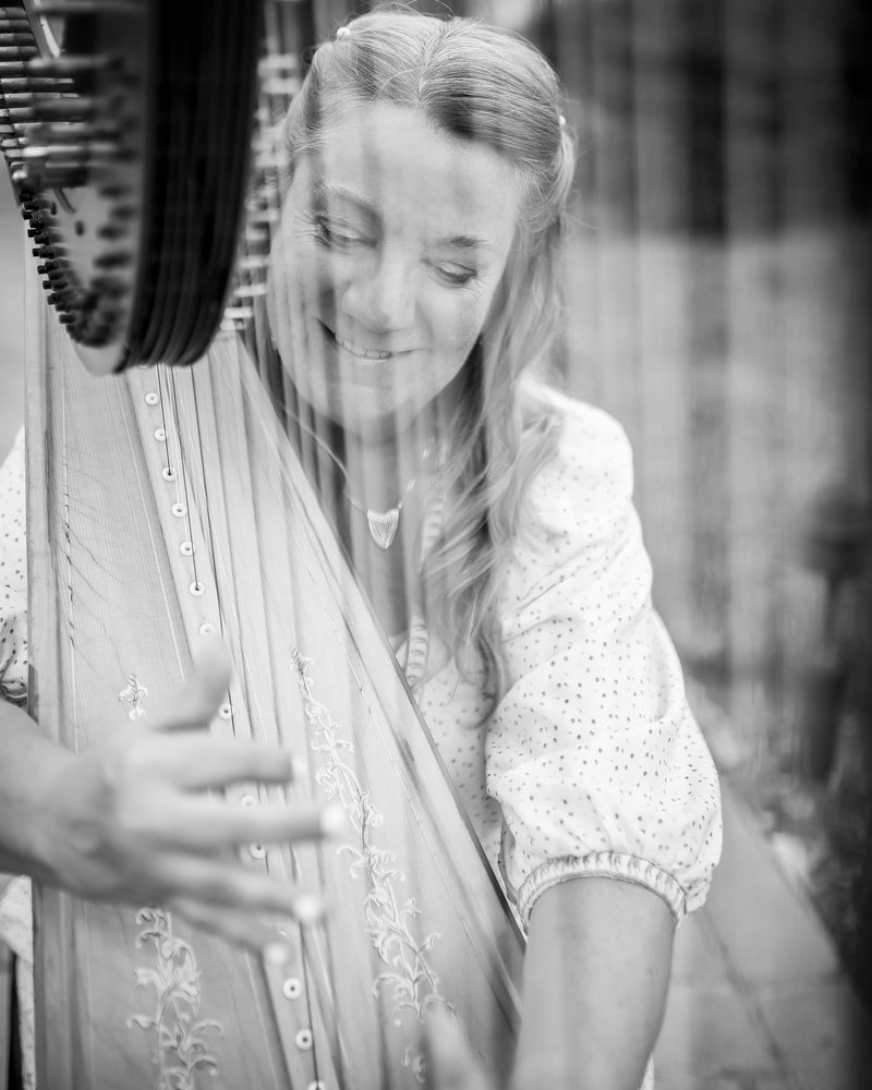 Patricia smiling as she plays, seen through the harp strings